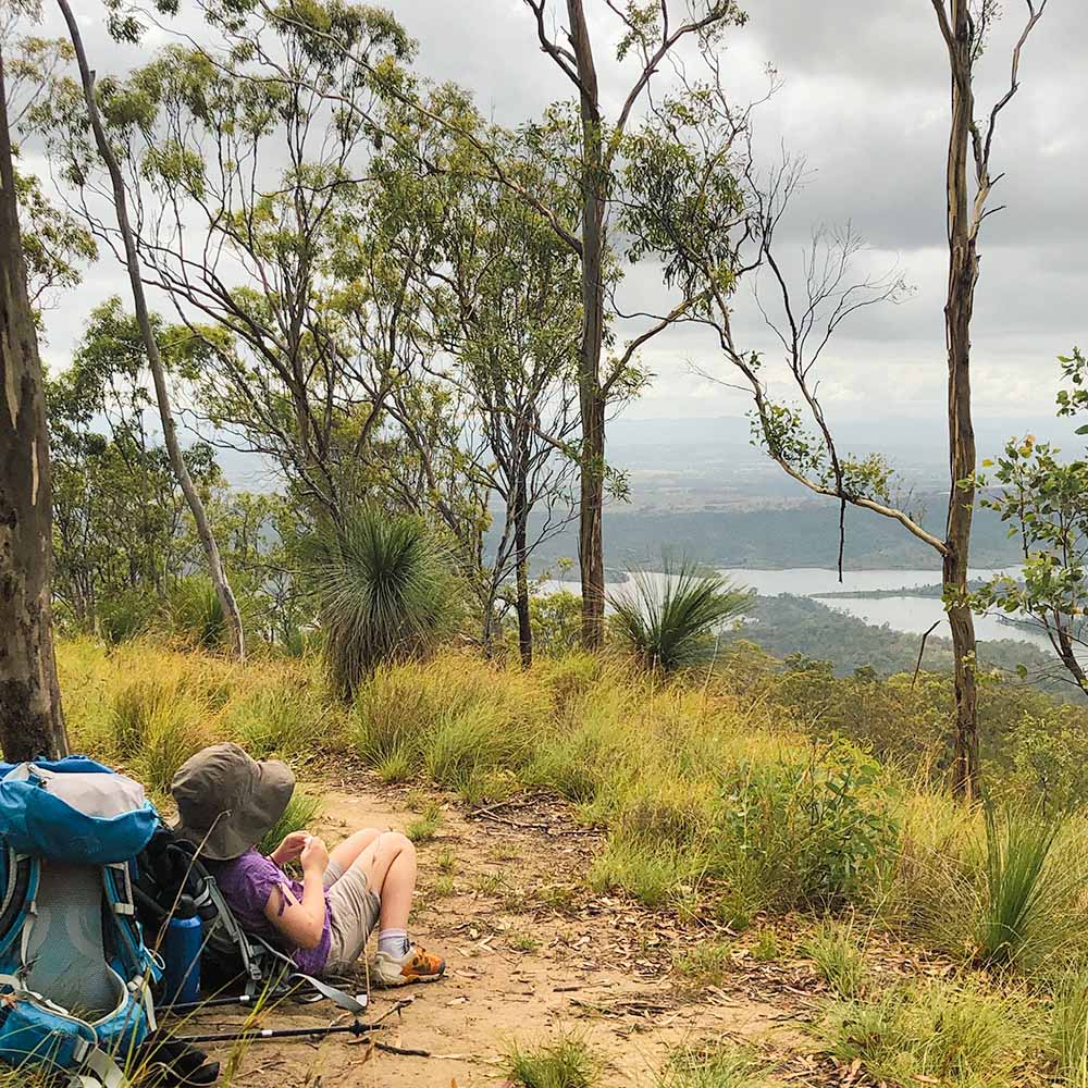 Child sitting relaxing against a tree on top of Mount Joyce, overlooking Wyaralong Dam